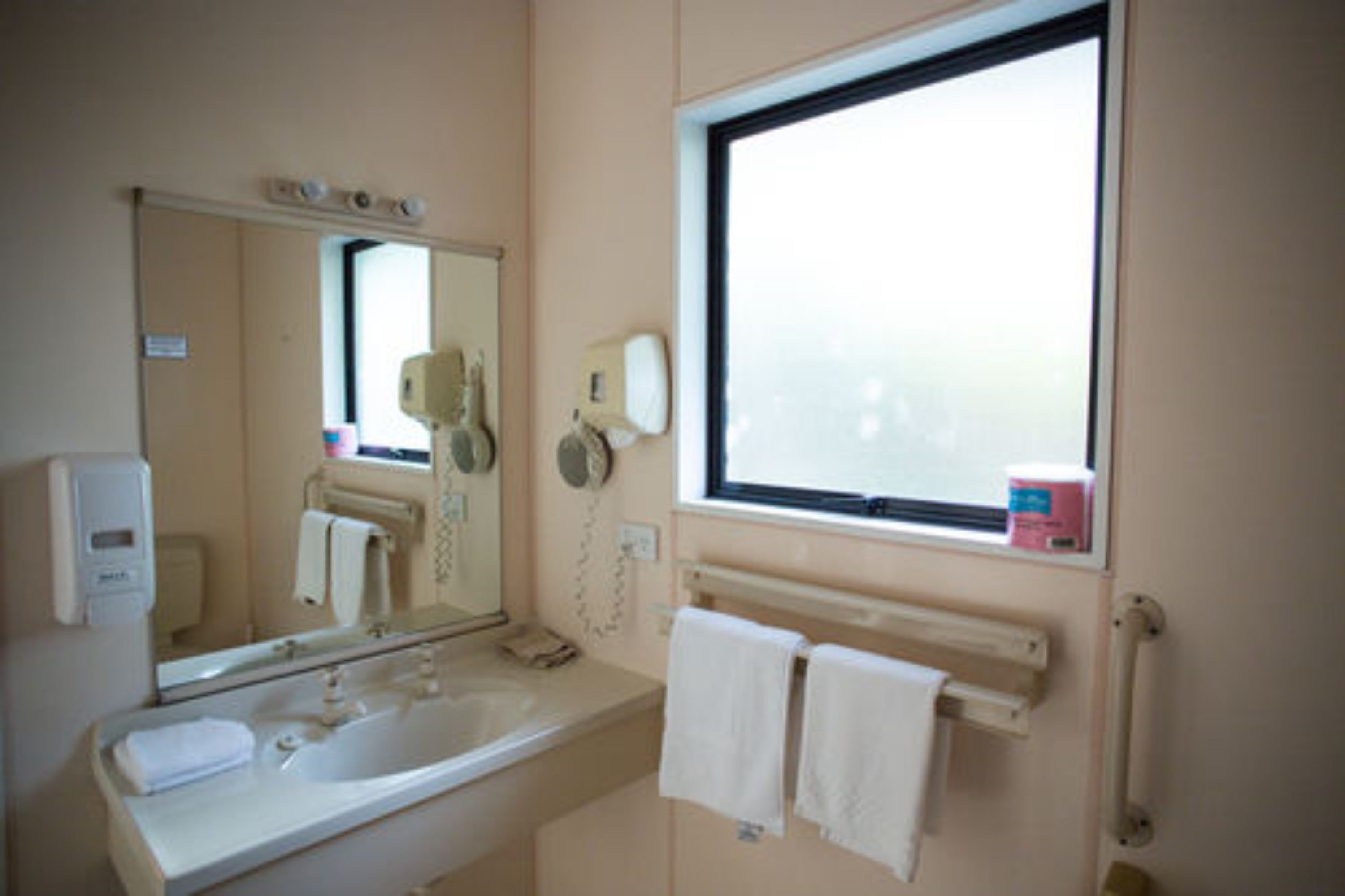 Une salle de bain équipée d’un lavabo, d’un miroir, d’un porte-serviettes et d’une fenêtre.