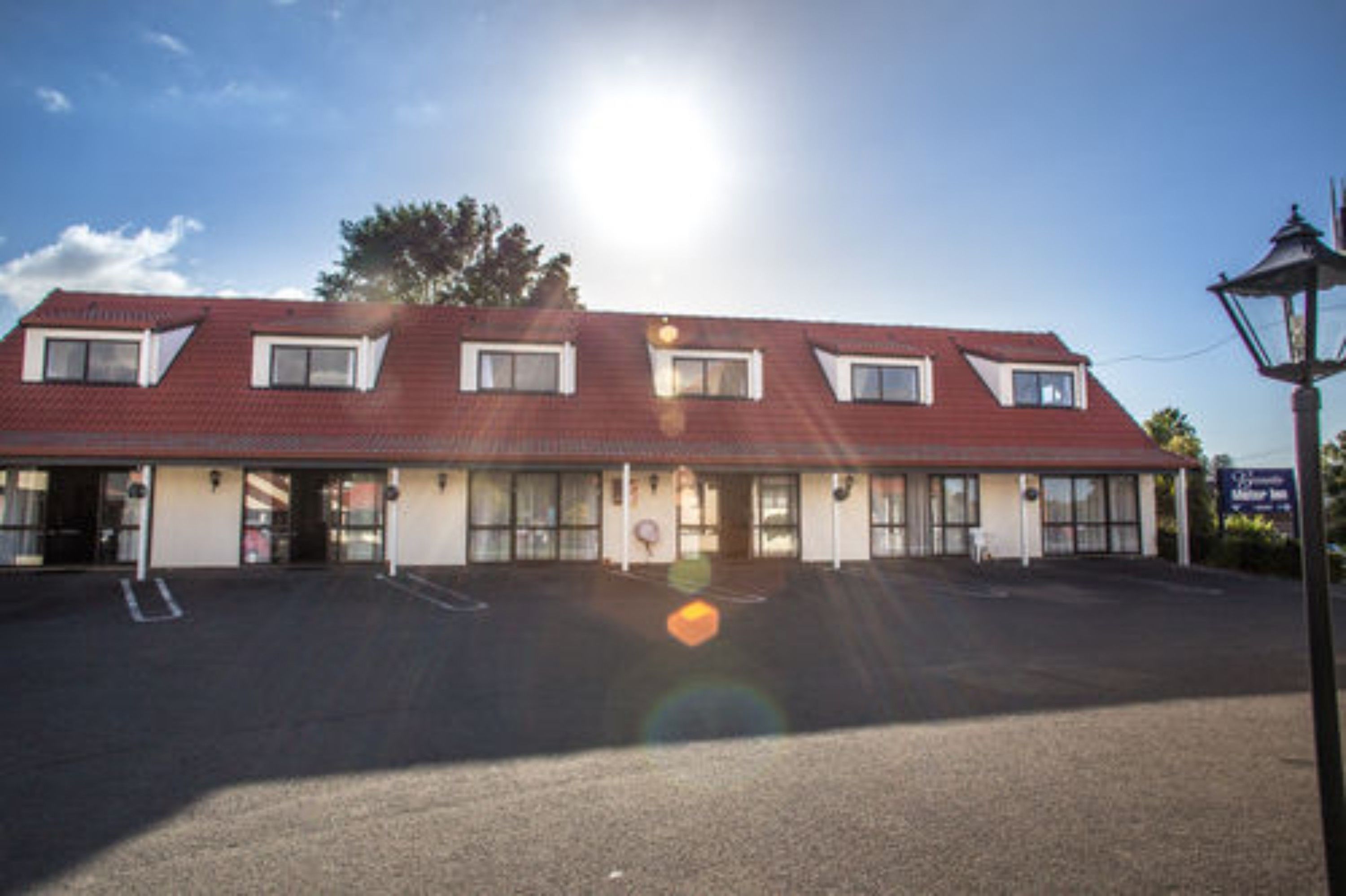 A two-story motel with a red roof, multiple windows, and a parking lot.