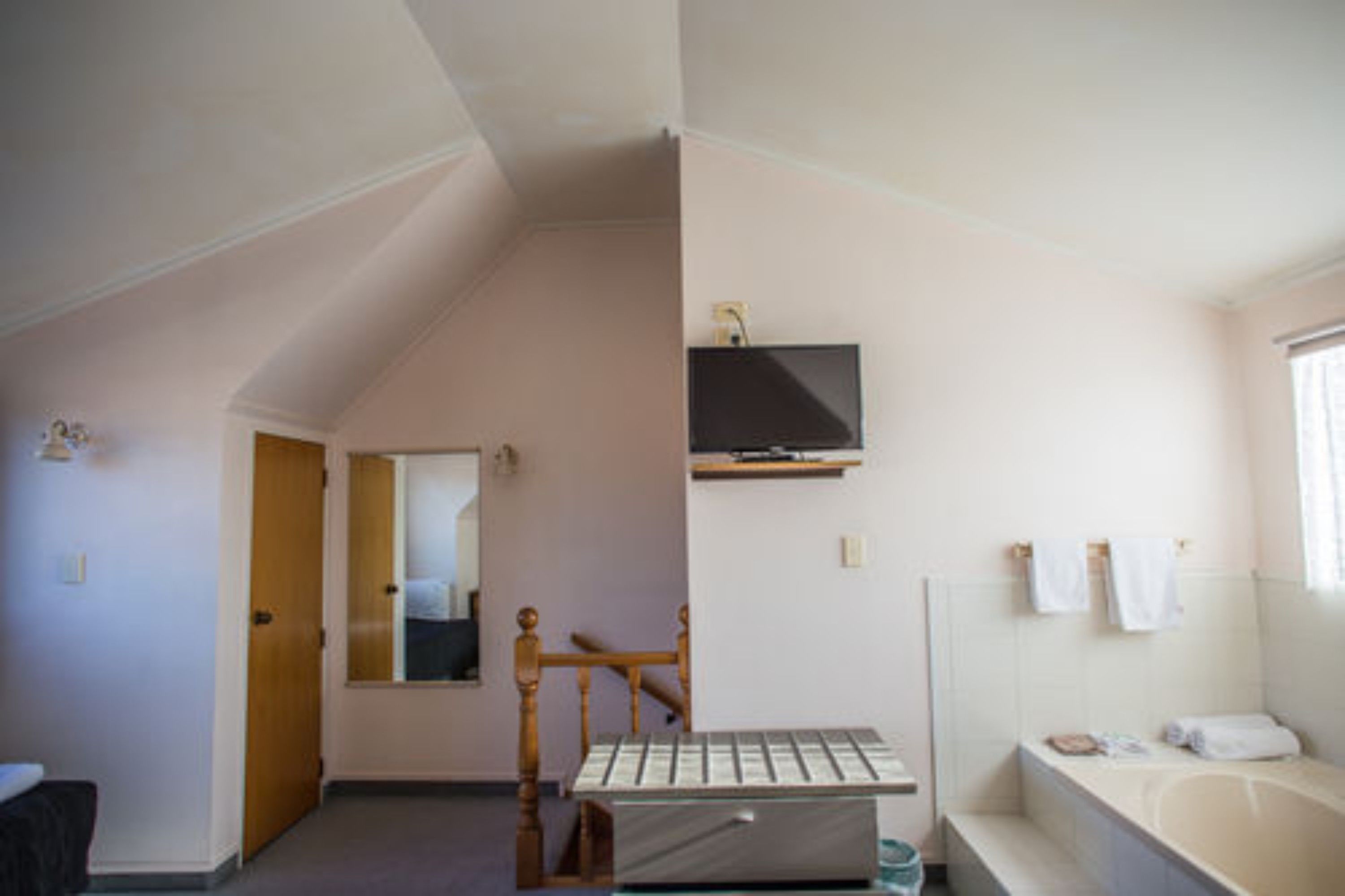 Une chambre avec un lit en bois, un téléviseur fixé au mur et une salle de bain avec une baignoire et des serviettes.
