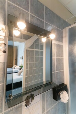A bathroom with a large mirror, three lights, a glass shelf, and a towel dispenser. - Nouvel Hôtel Paris (Paris)