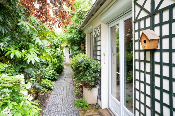 A narrow brick pathway leading to a building with a white facade and green window frames. There is a birdhouse mounted on the wall. - Nouvel Hôtel Paris (Paris)