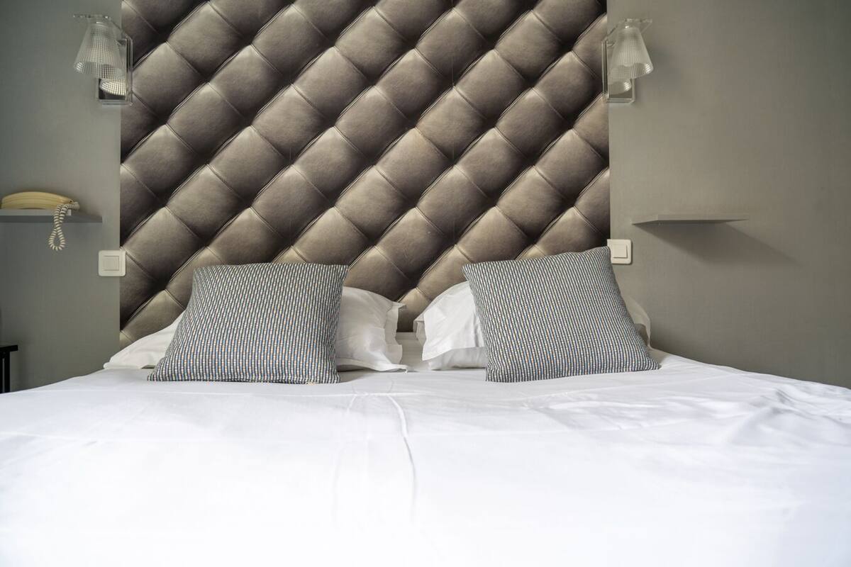 Habitación de hotel con cabecera capitonada, dos lámparas de noche y una cama bien hecha con almohadas a rayas.