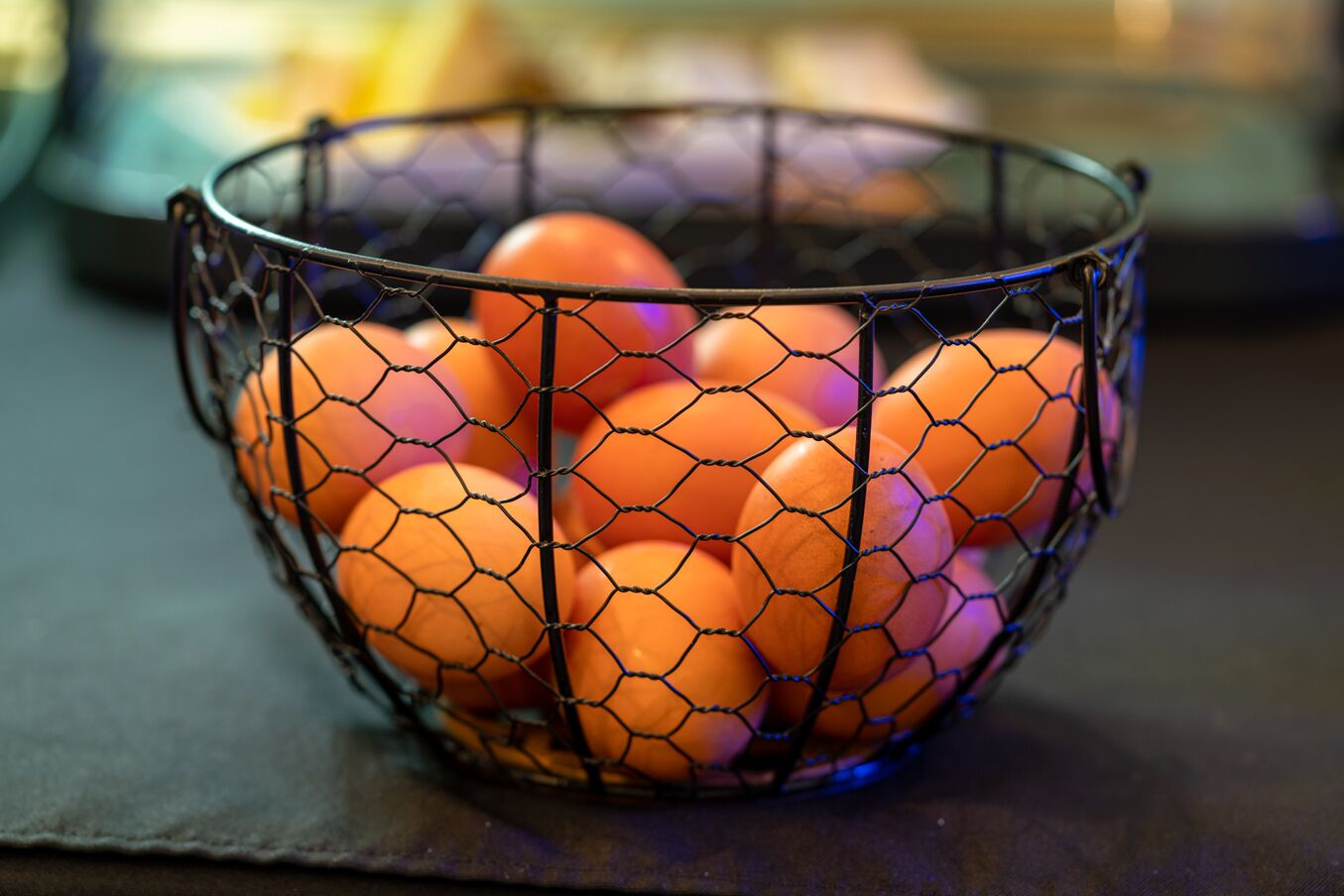A wire basket containing several oranges on a dark surface.