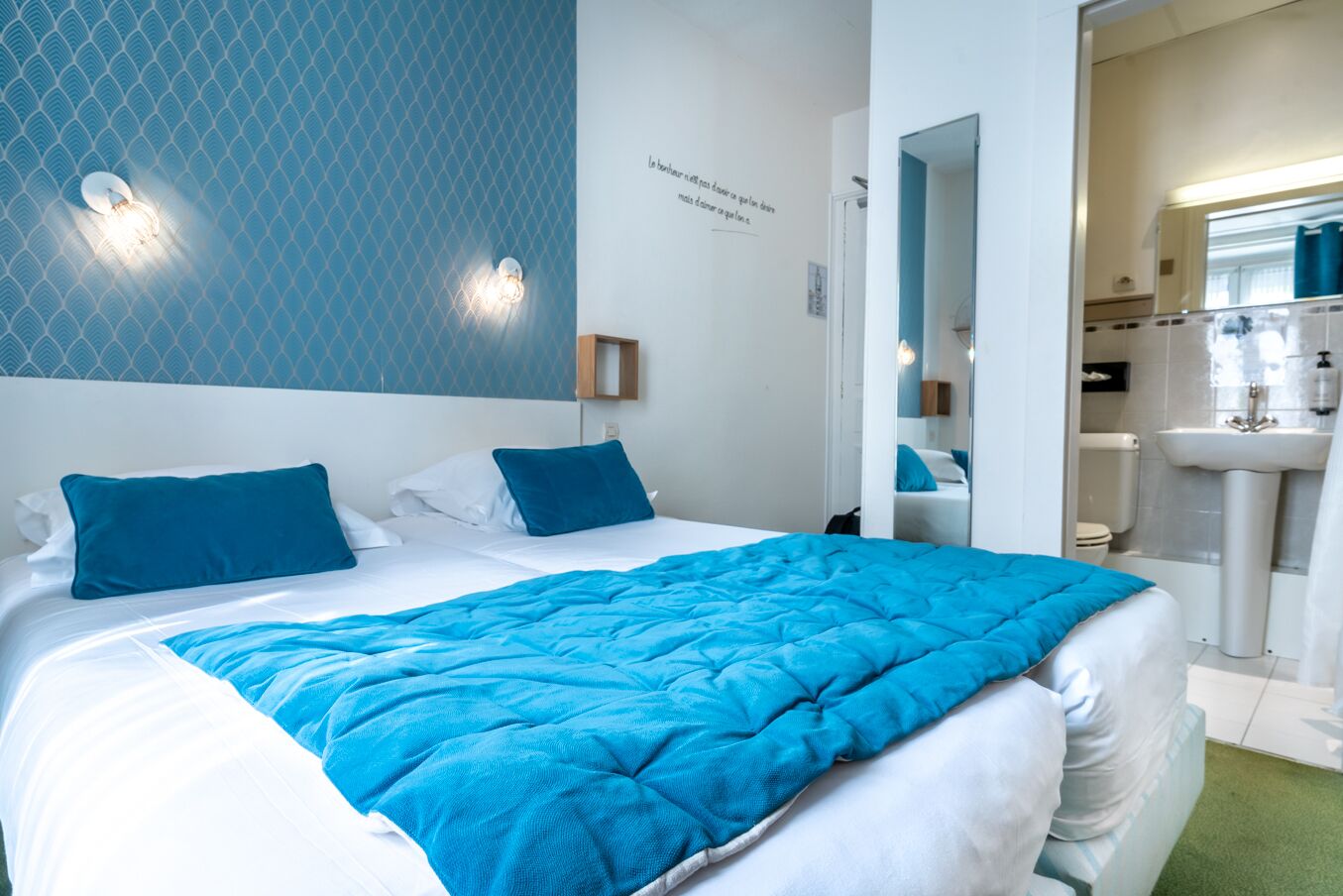 A hotel room with a large bed, a bathroom with a sink and mirror, and a blue patterned wall.