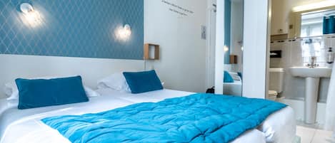 A hotel room with a large bed, a bathroom with a sink and mirror, and a blue patterned wall.