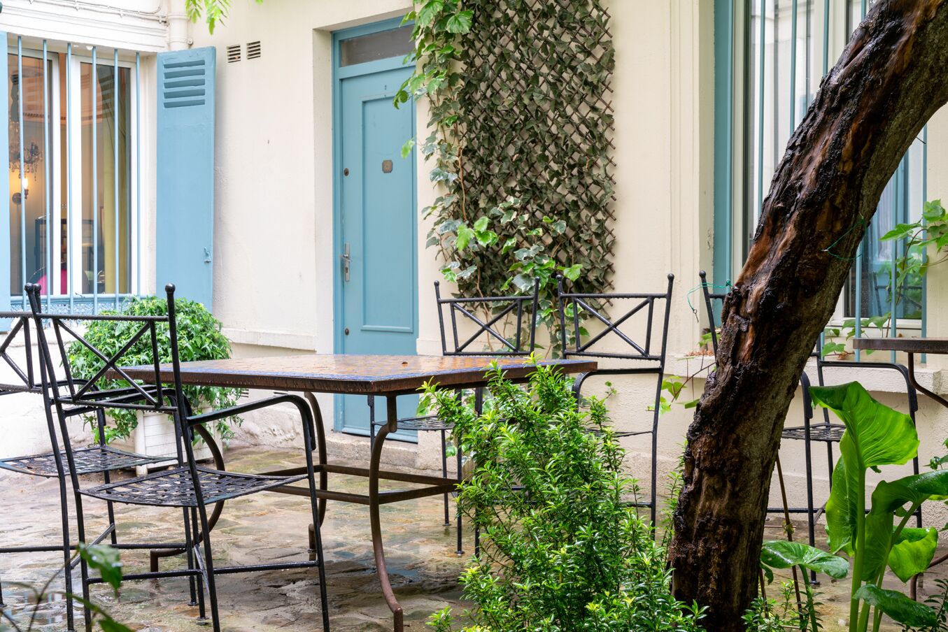 An outdoor seating area with metal chairs and tables, a blue door, and a vine-covered wall.