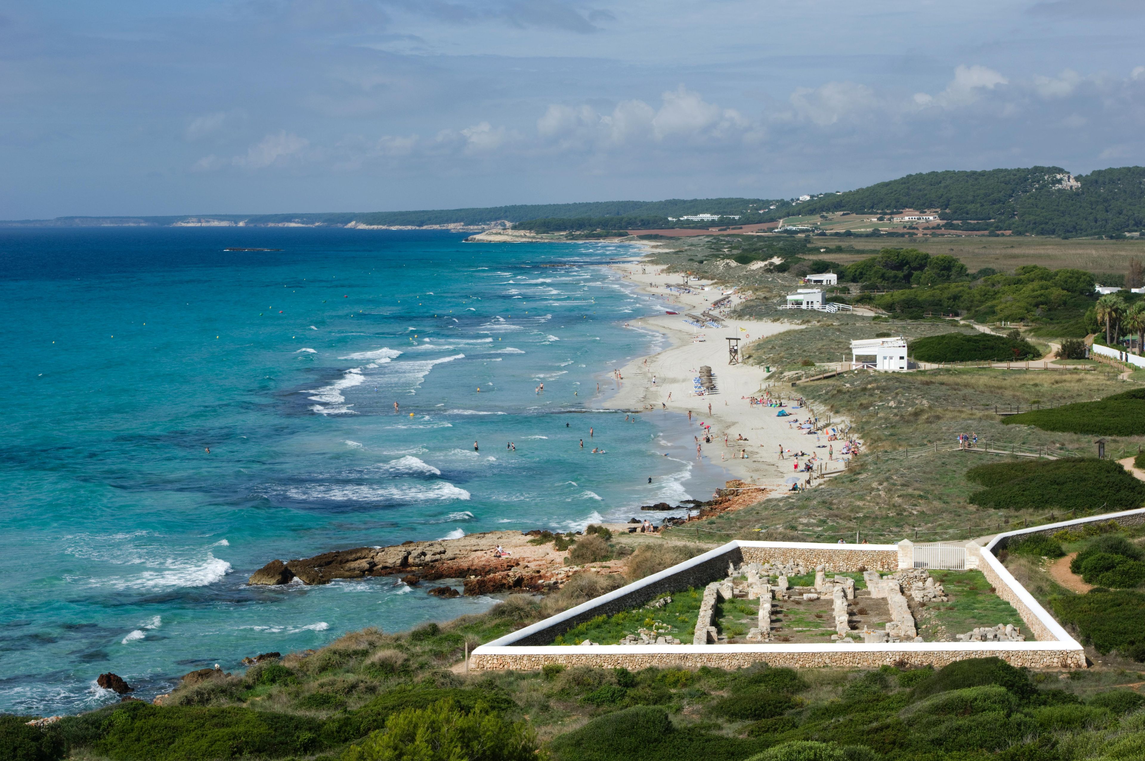 Una playa costera con aguas azules cristalinas, un litoral arenoso y una estructura de piedra en primer plano.