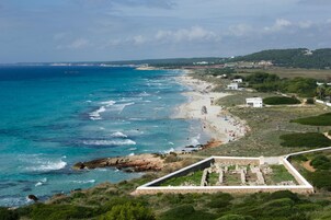 Una playa costera con aguas azules cristalinas, un litoral arenoso y una estructura de piedra en primer plano.