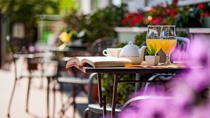 An outdoor table with a book, teapot, cups, and a glass of orange juice. - Hotel Virginia (Diano Marina)