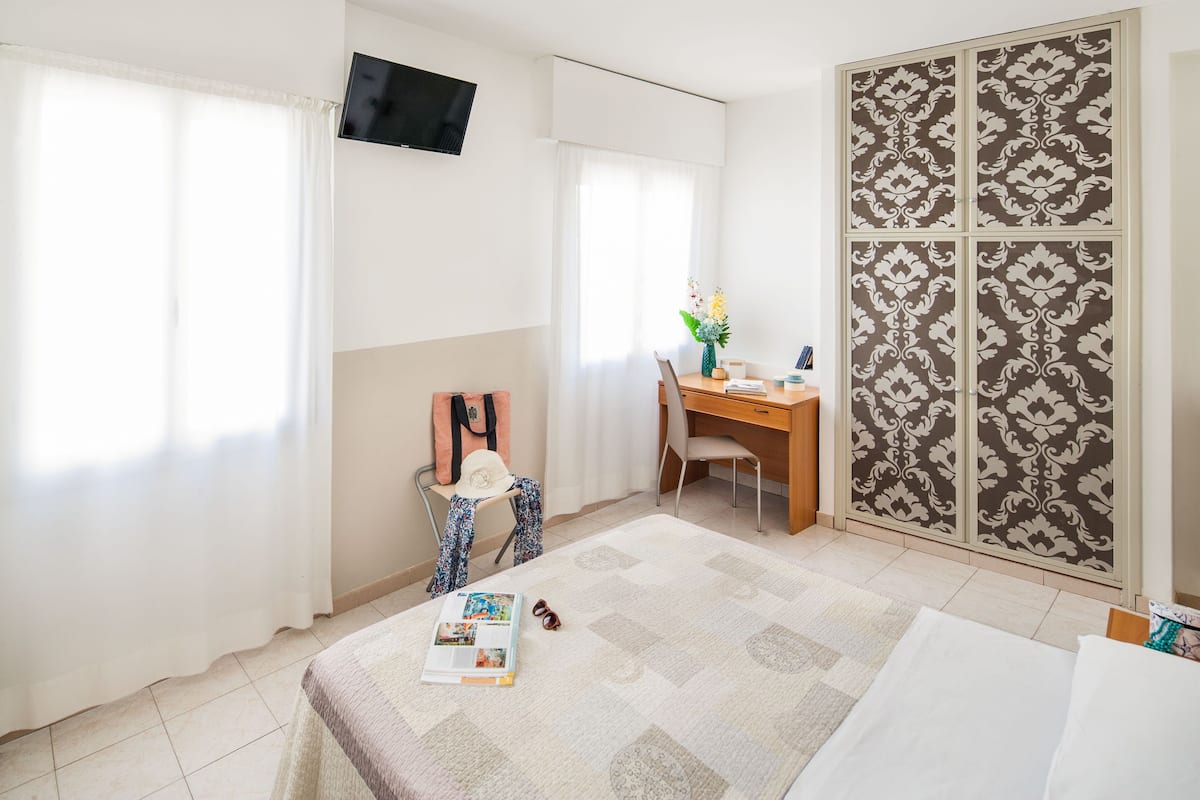 A bedroom with a bed, a desk, a chair, a TV, and a wardrobe.