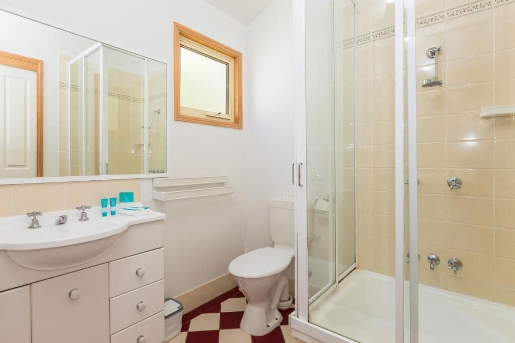 Une salle de bain avec un lavabo blanc, un miroir, des toilettes et une douche à parois de verre.