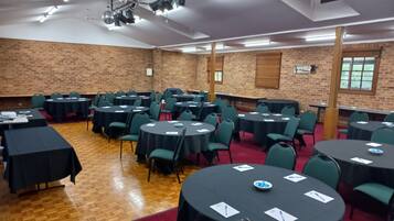 Uma sala de conferências com várias mesas redondas, cadeiras verdes e uma parede de tijolos.