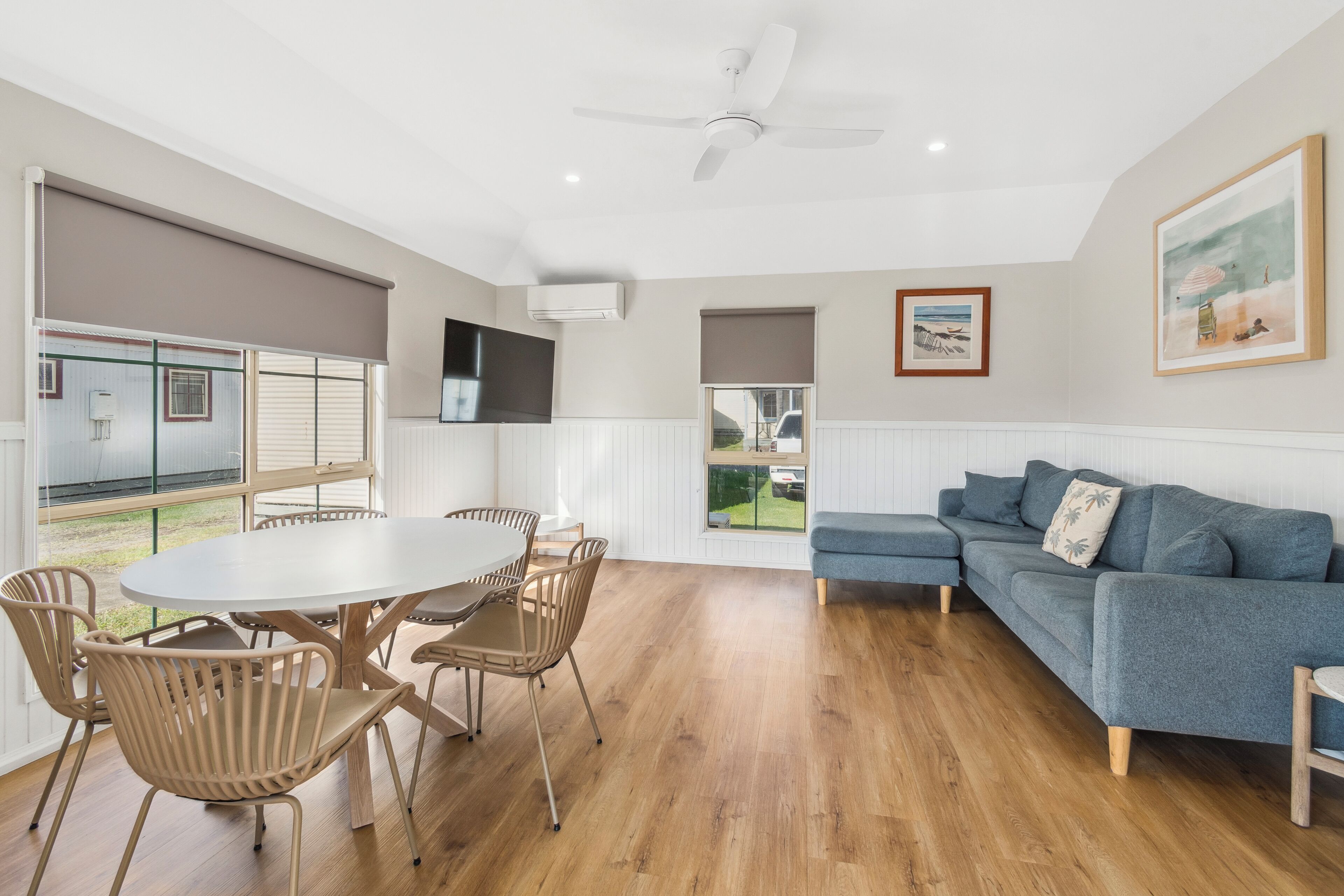 Un salon moderne avec une table à manger ronde, des chaises de couleur beige, un canapé bleu et un ventilateur de plafond.