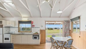 Cocina amplia con armarios blancos, estufa y microondas. Hay un comedor con mesa y sillas, y un gran ventanal con vistas al exterior.