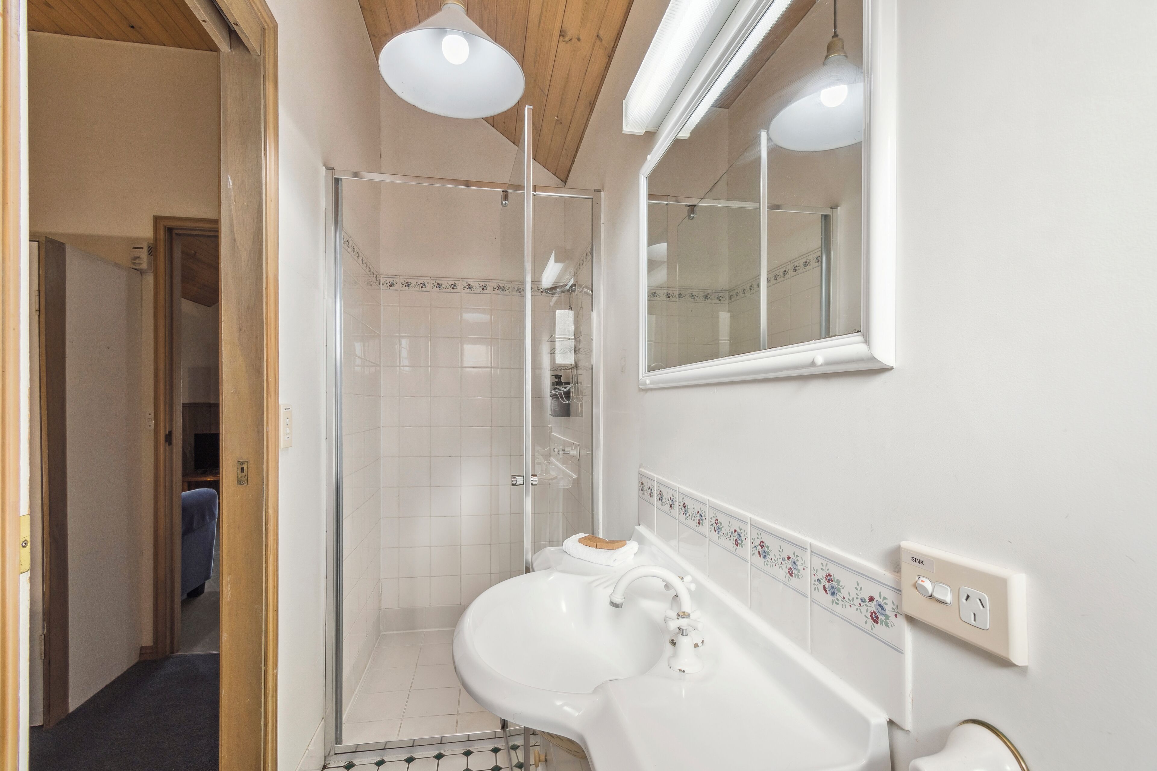 Un baño con un lavamanos blanco, un espejo y una zona de ducha.
