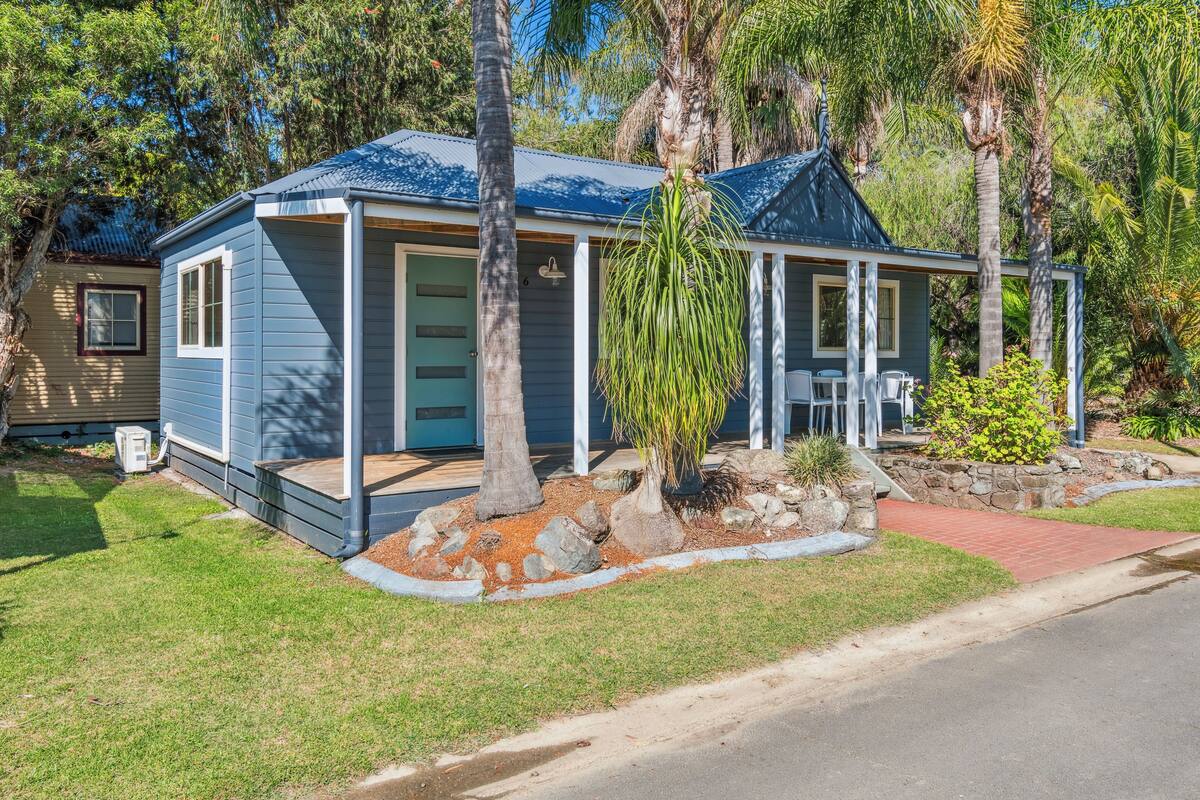 A single-story house with a blue roof and white siding, surrounded by a well-maintained lawn and palm trees.
