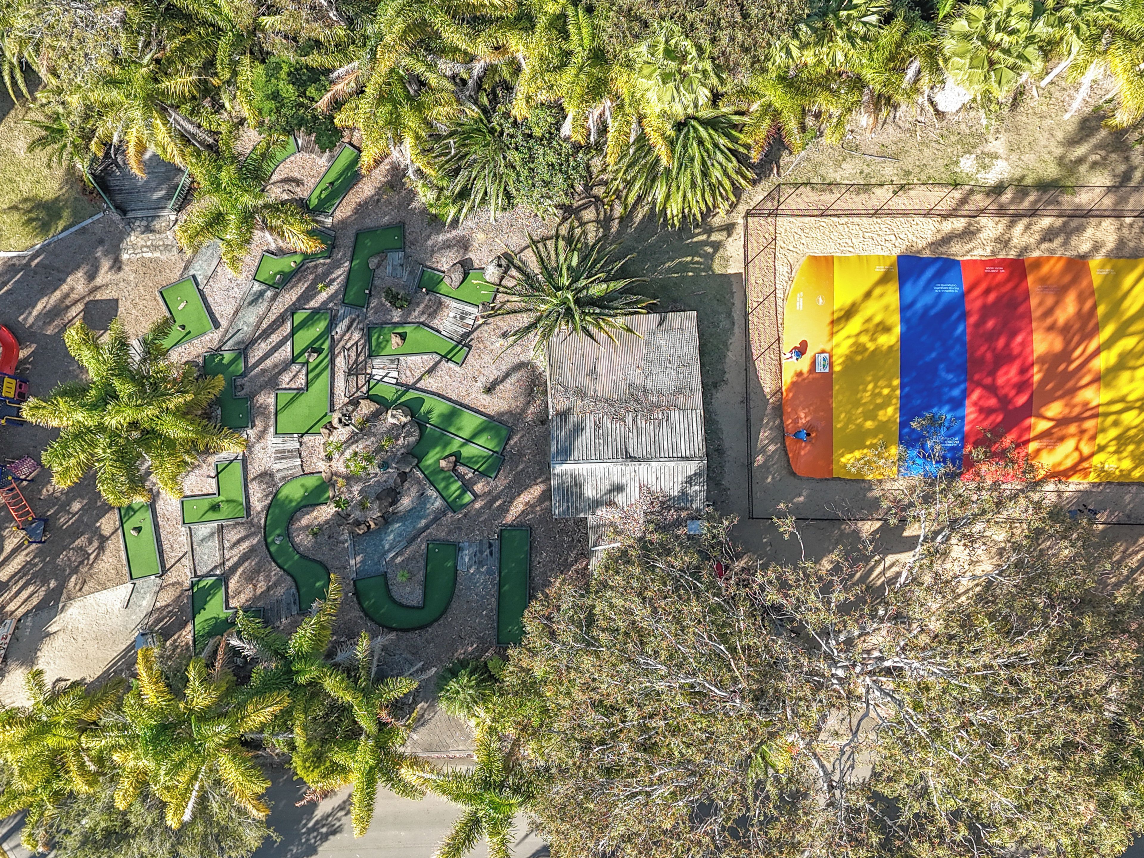 Luchtbeeld van een golfbaan met een groot bord waarop 'GOLF' staat en een kleurrijke muur aan de rechterkant.