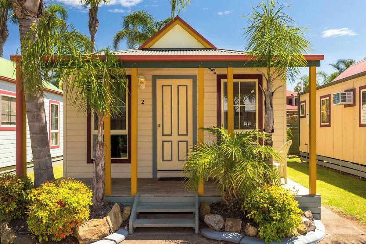 A small, single-story building with a porch, surrounded by palm trees and other greenery.