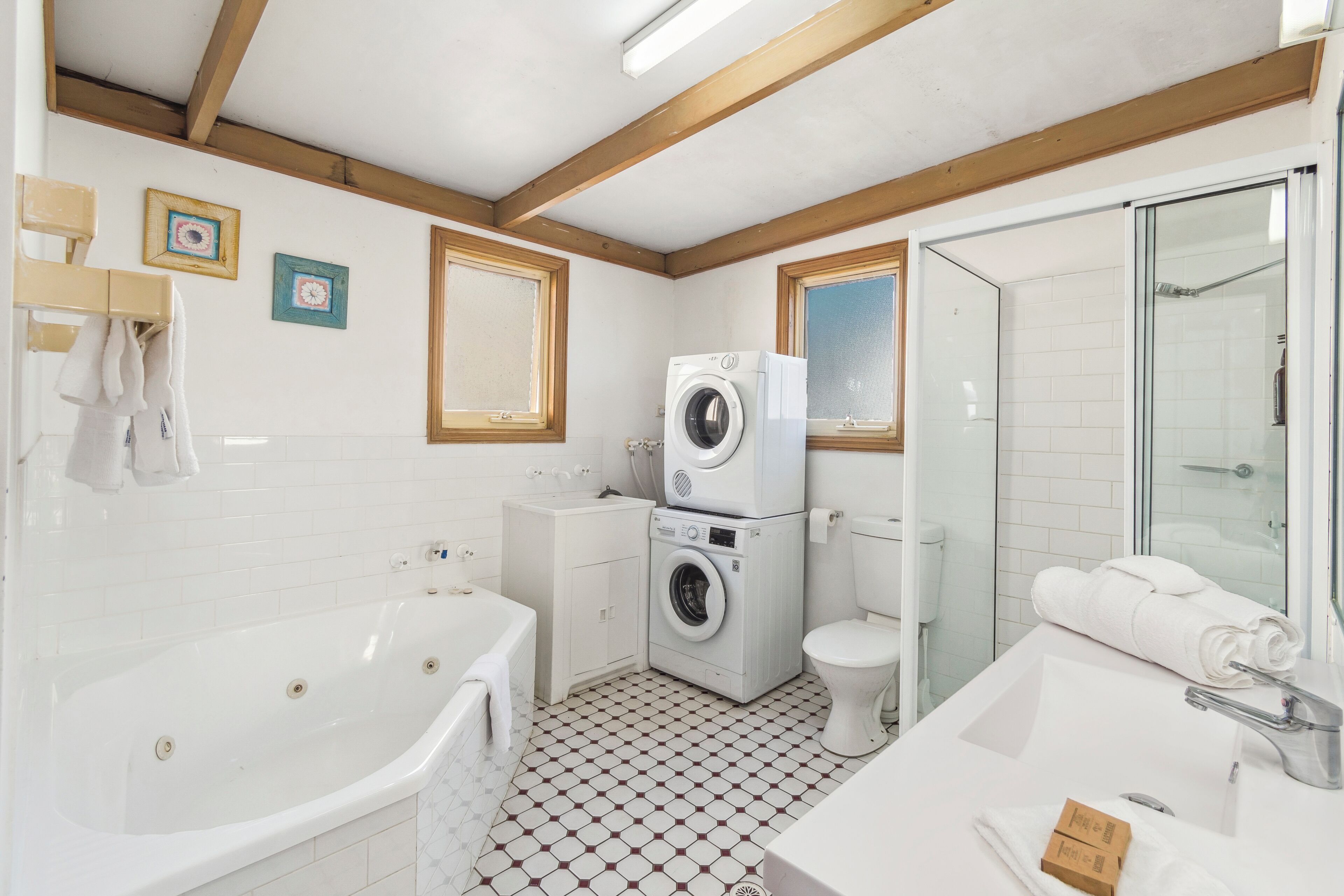 A modern bathroom with a bathtub, a washing machine, a toilet, and a glass shower enclosure.