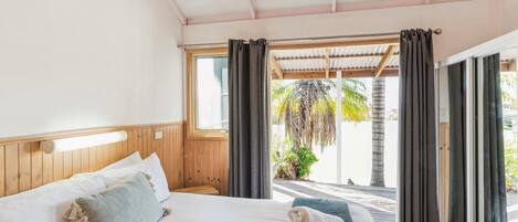A bedroom with a bed, a ceiling fan, a window, and a view of palm trees.