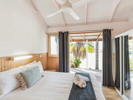 Une chambre avec un lit, un ventilateur de plafond, une fenêtre et une vue sur des palmiers.