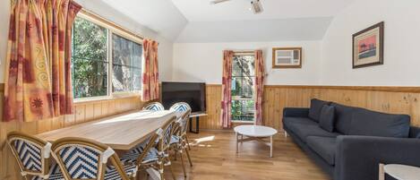 A room with a wooden dining table, chairs, a sofa, a television, and a ceiling fan.