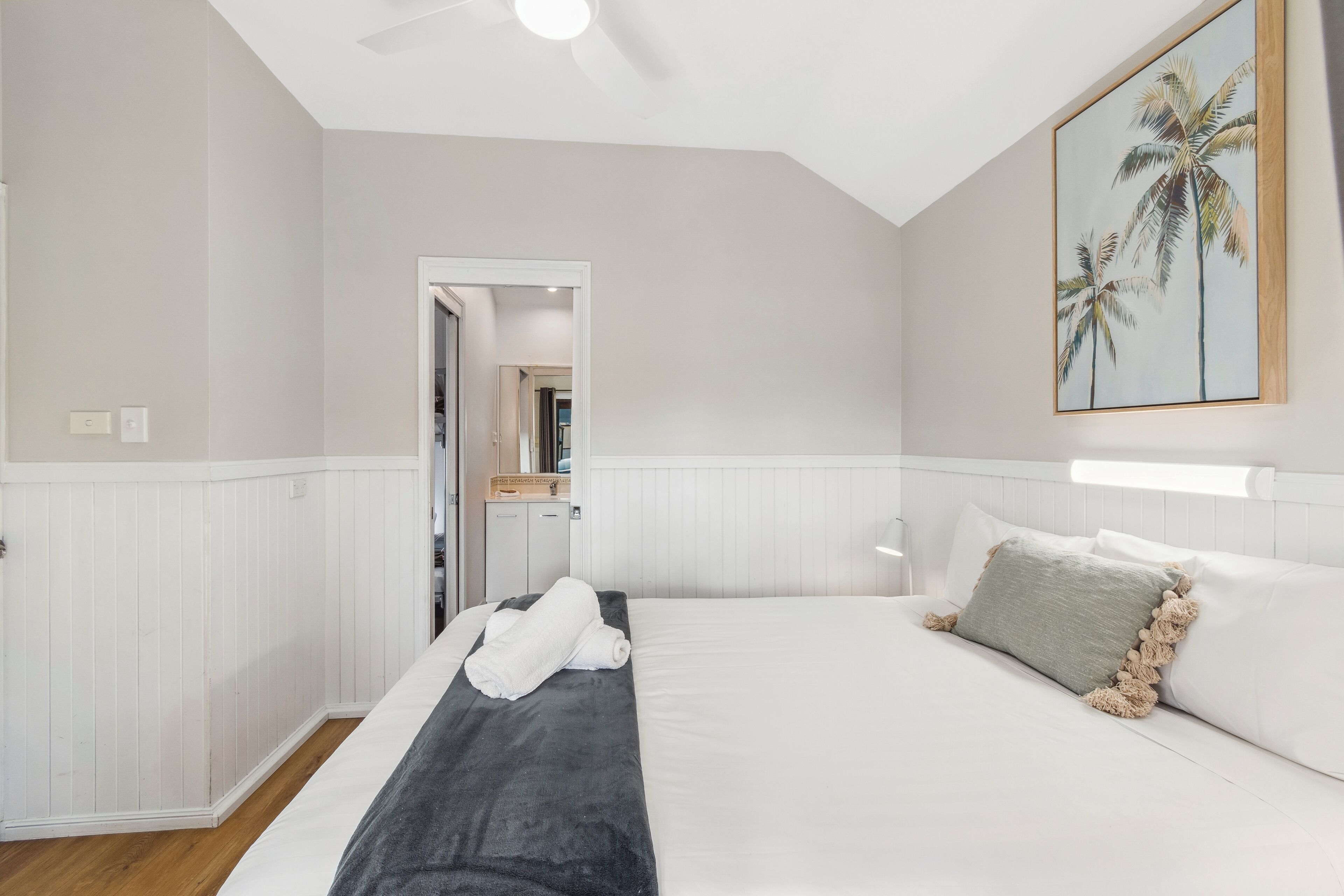 A hotel room with a bed, a door leading to a bathroom, and a painting of palm trees on the wall.