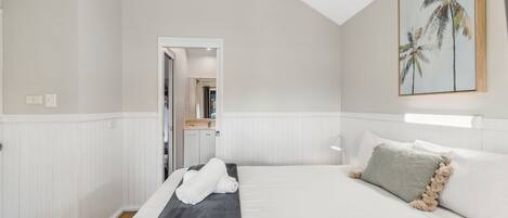 A hotel room with a bed, a door leading to a bathroom, and a painting of palm trees on the wall.
