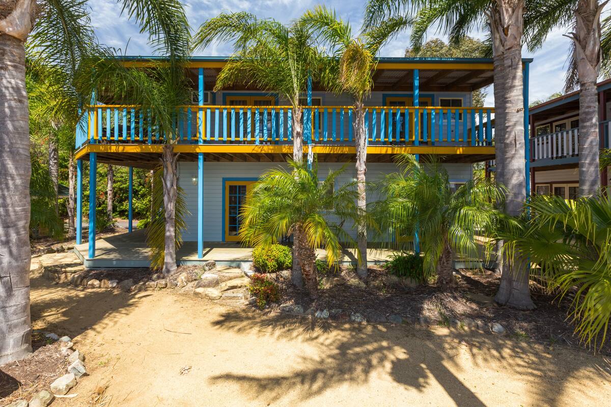 A two-story building with blue balconies and palm trees.