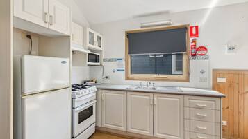 Una cocina con armarios blancos, estufa, microondas y ventana.