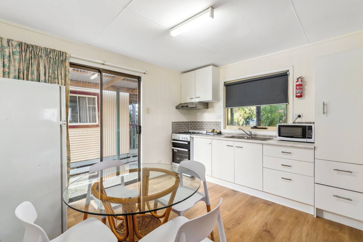 A modern kitchen with white cabinets, a glass dining table, and a microwave.