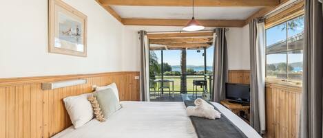 Un dormitorio con una cama grande, cabecera de madera, televisor sobre una mesita auxiliar y vistas al exterior a través de una puerta de cristal.