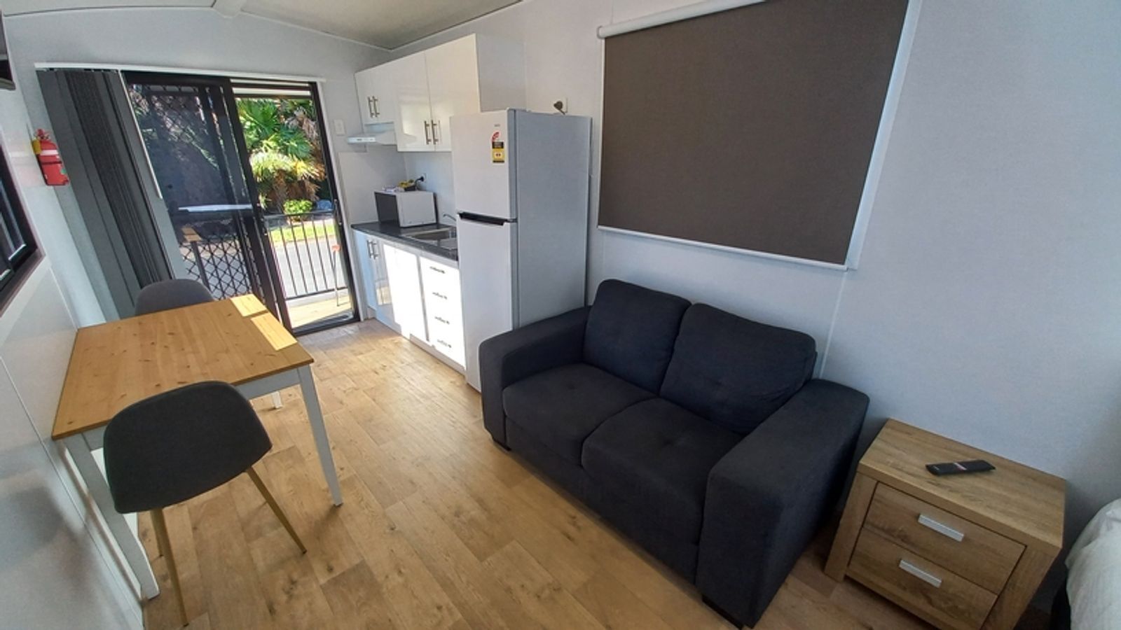 Ein kompakter Wohnraum mit Küchenzeile, einer Couch, einem Esstisch mit Stühlen und einem kleinen Nachttisch.
