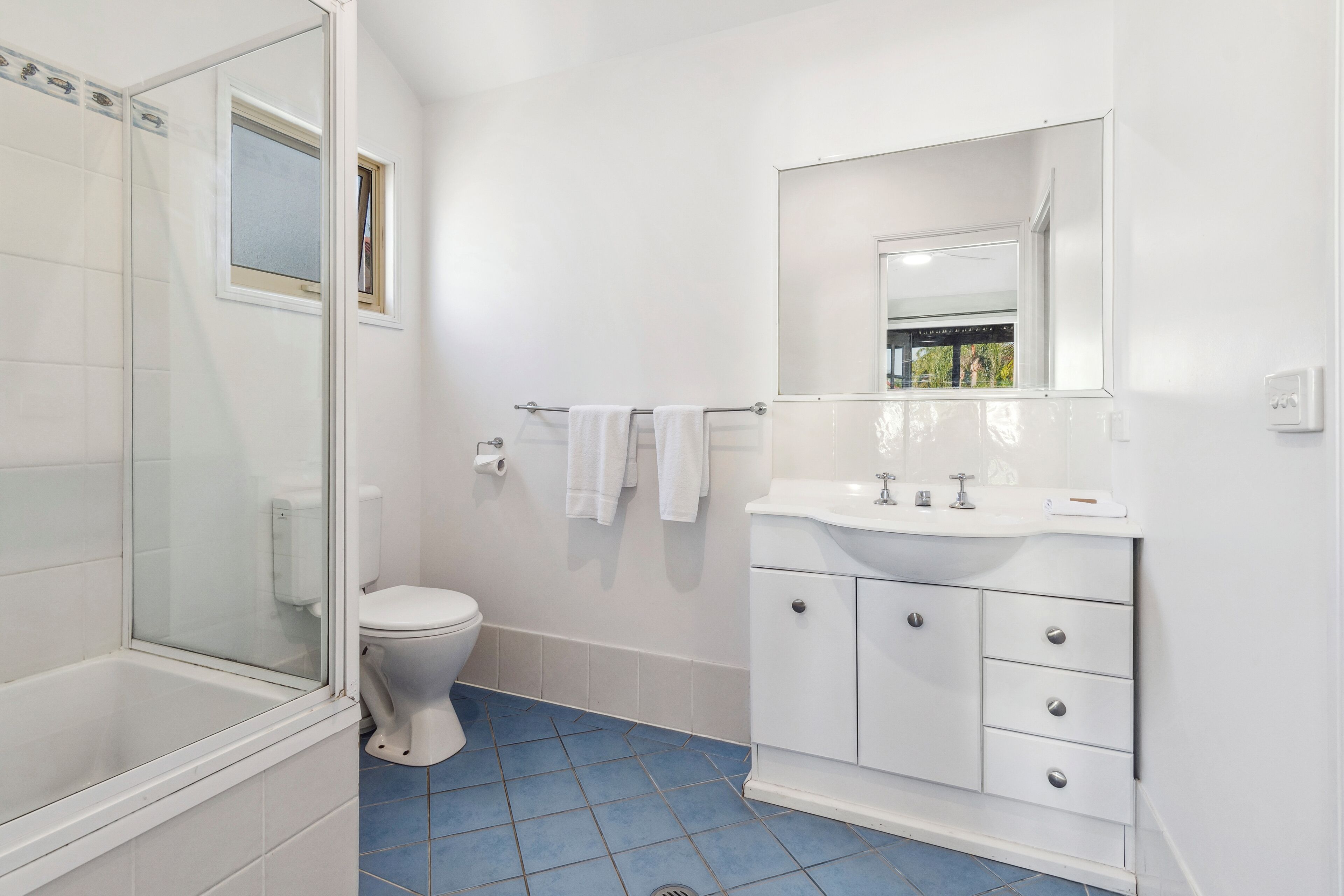 A bathroom with a glass-enclosed shower, a white toilet, a sink with a mirror, and blue-tiled flooring.