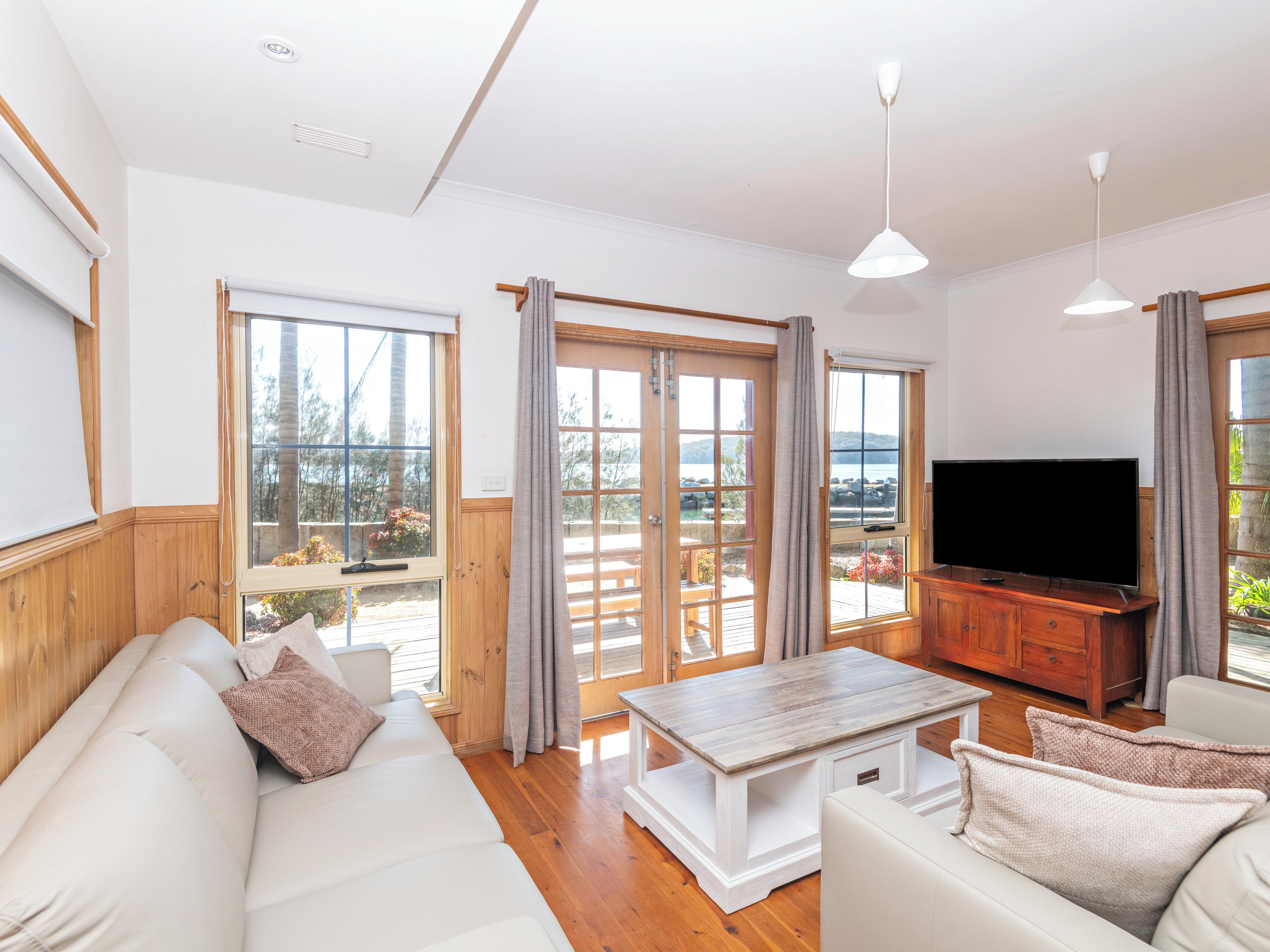 A living room with a sofa, a coffee table, a TV, and a view of the outdoors through large windows.