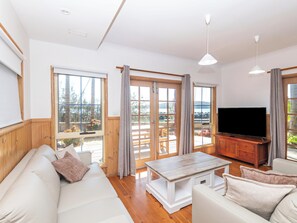 Una sala de estar con un sofá, una mesa de centro, un televisor y vistas al exterior a través de amplias ventanas.