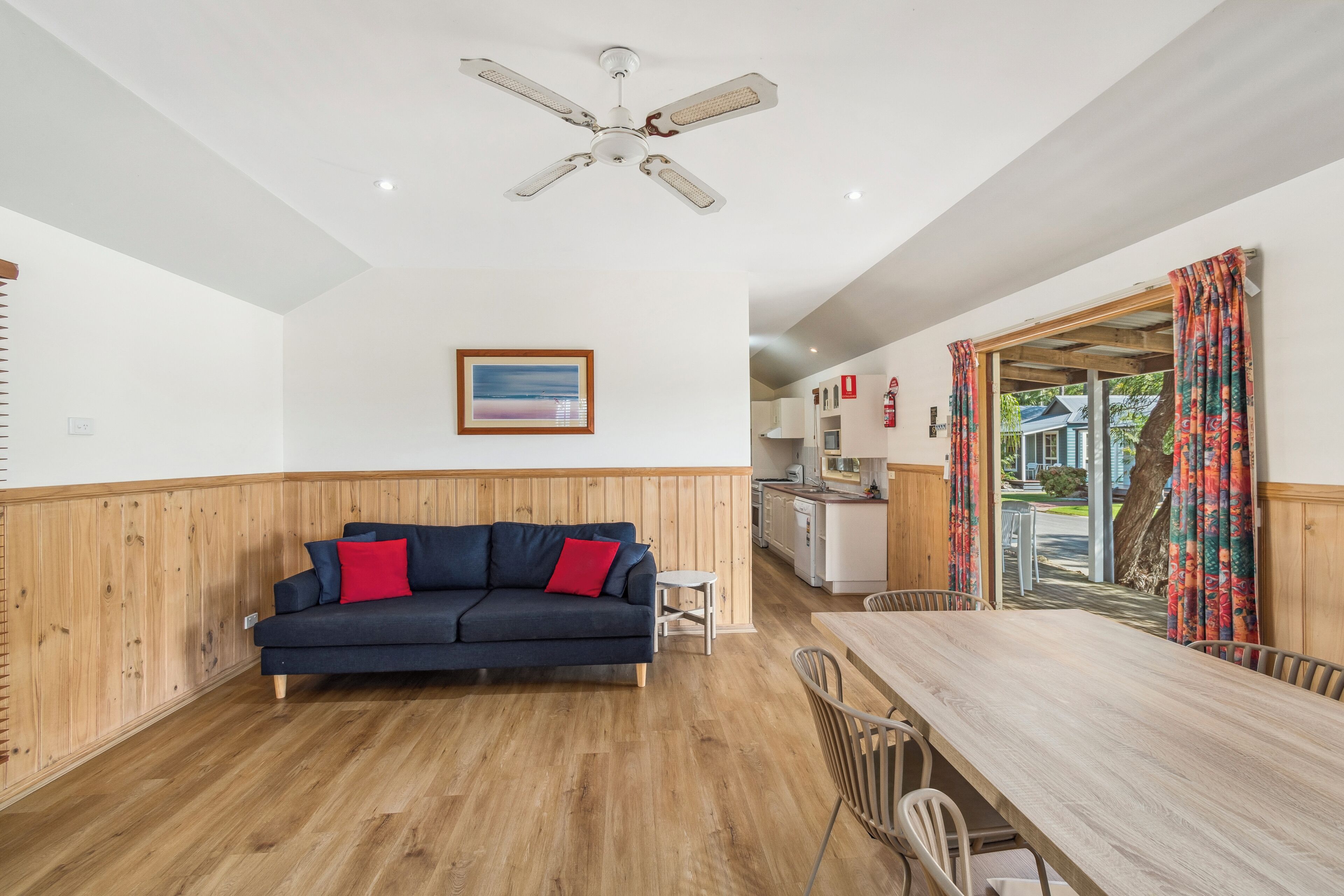 A modern living room with a dark blue sofa, a wooden dining table, and a ceiling fan.