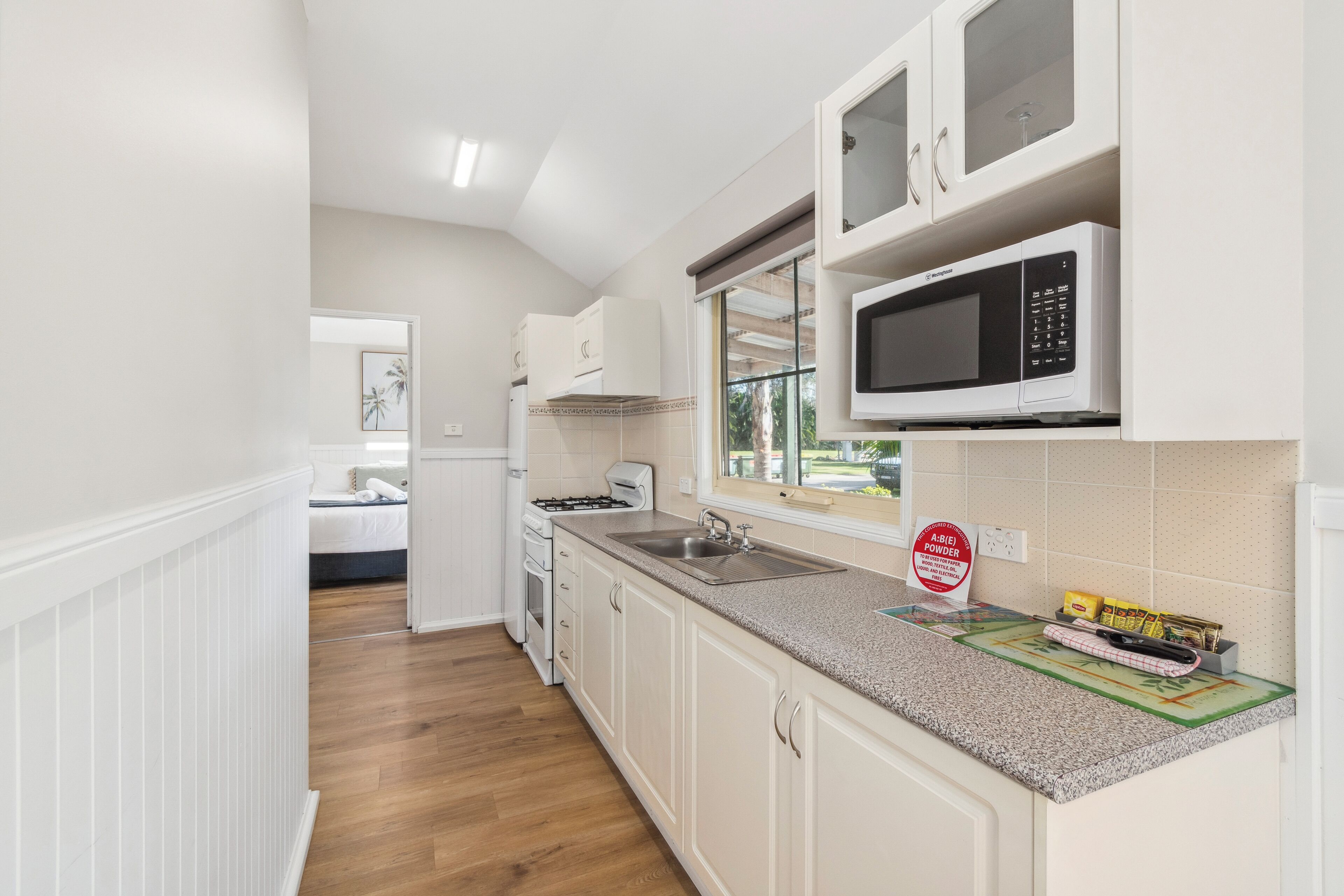 A compact kitchen with white cabinetry, a microwave, a gas stove, and a window.
