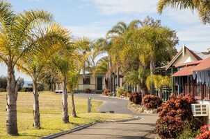 A pathway leading to a building with a red roof, surrounded by palm trees and shrubs.