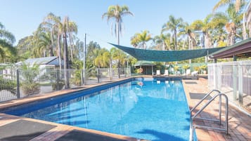 A swimming pool with a shaded area, surrounded by palm trees and a fenced deck.