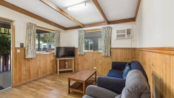 Quarto com paredes de madeira, televisão sobre suporte, sofá e janela com cortinas.