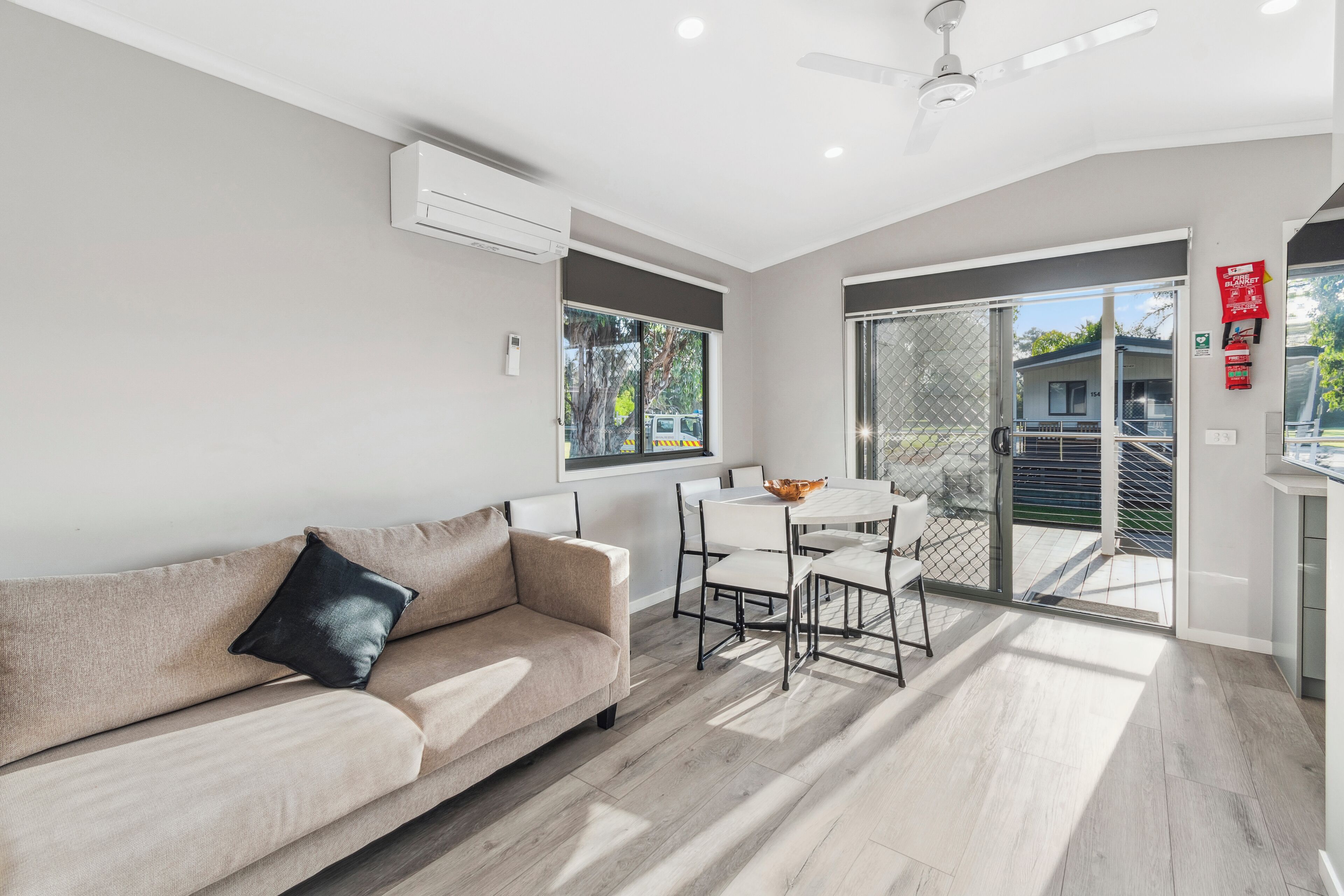 A modern living room with a beige sofa, a dining table with chairs, and a sliding glass door leading to a balcony.