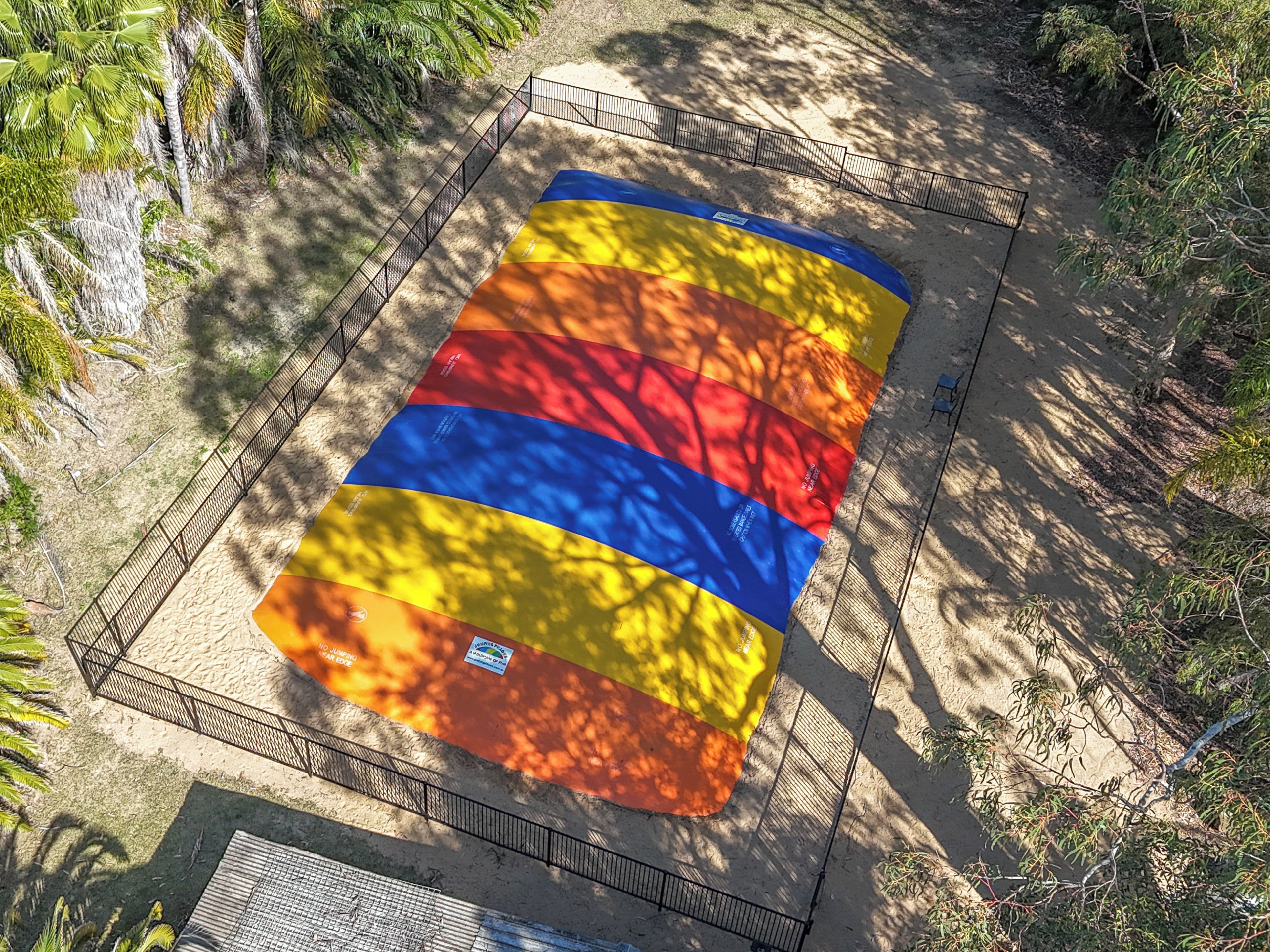 Vista aérea de una gran estructura inflable y colorida rodeada por una valla metálica, árboles y suelo arenoso.