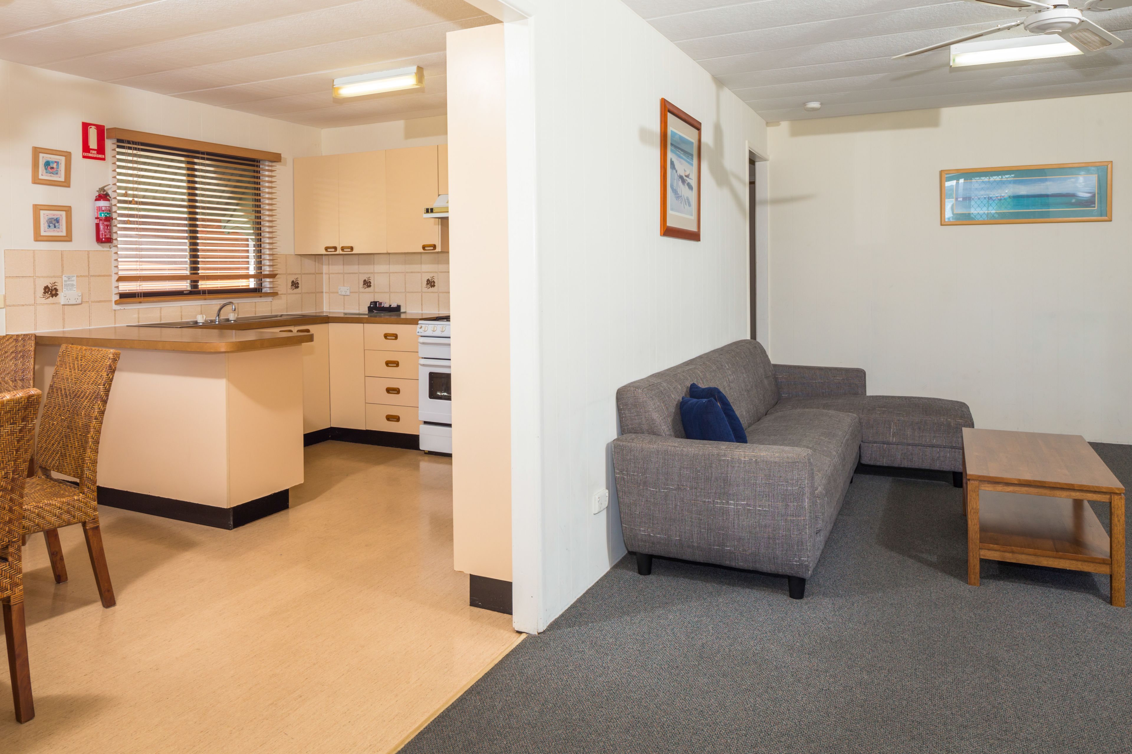 A compact living space with a kitchenette, a grey sofa, a wooden coffee table, and a wicker chair.