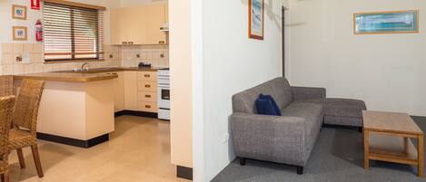 A compact living space with a kitchenette, a grey sofa, a wooden coffee table, and a wicker chair.