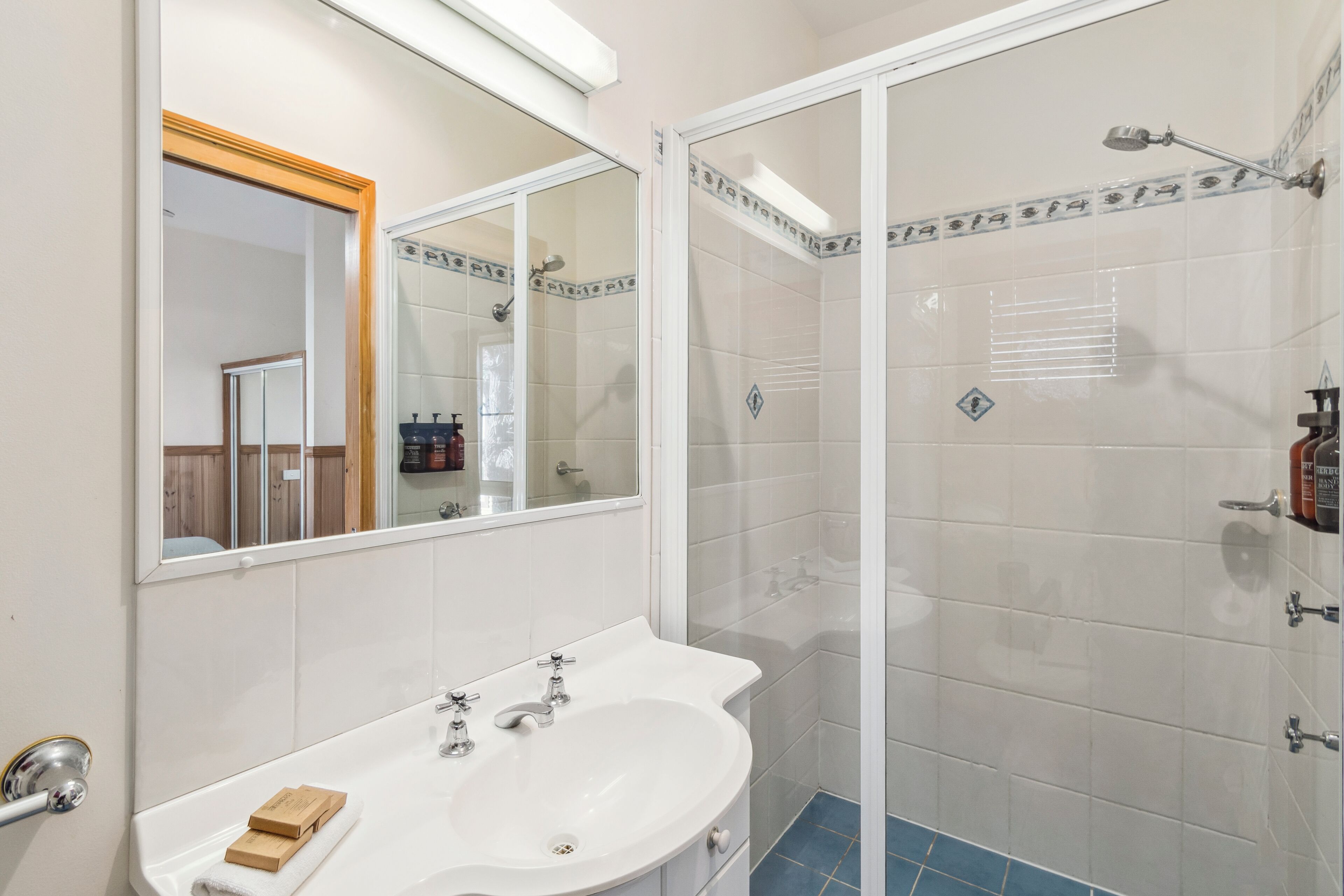 Un baño con lavamanos blanco, espejo y zona de ducha.