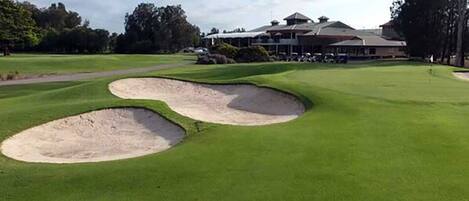 A golf course with bunkers and a clubhouse in the background.