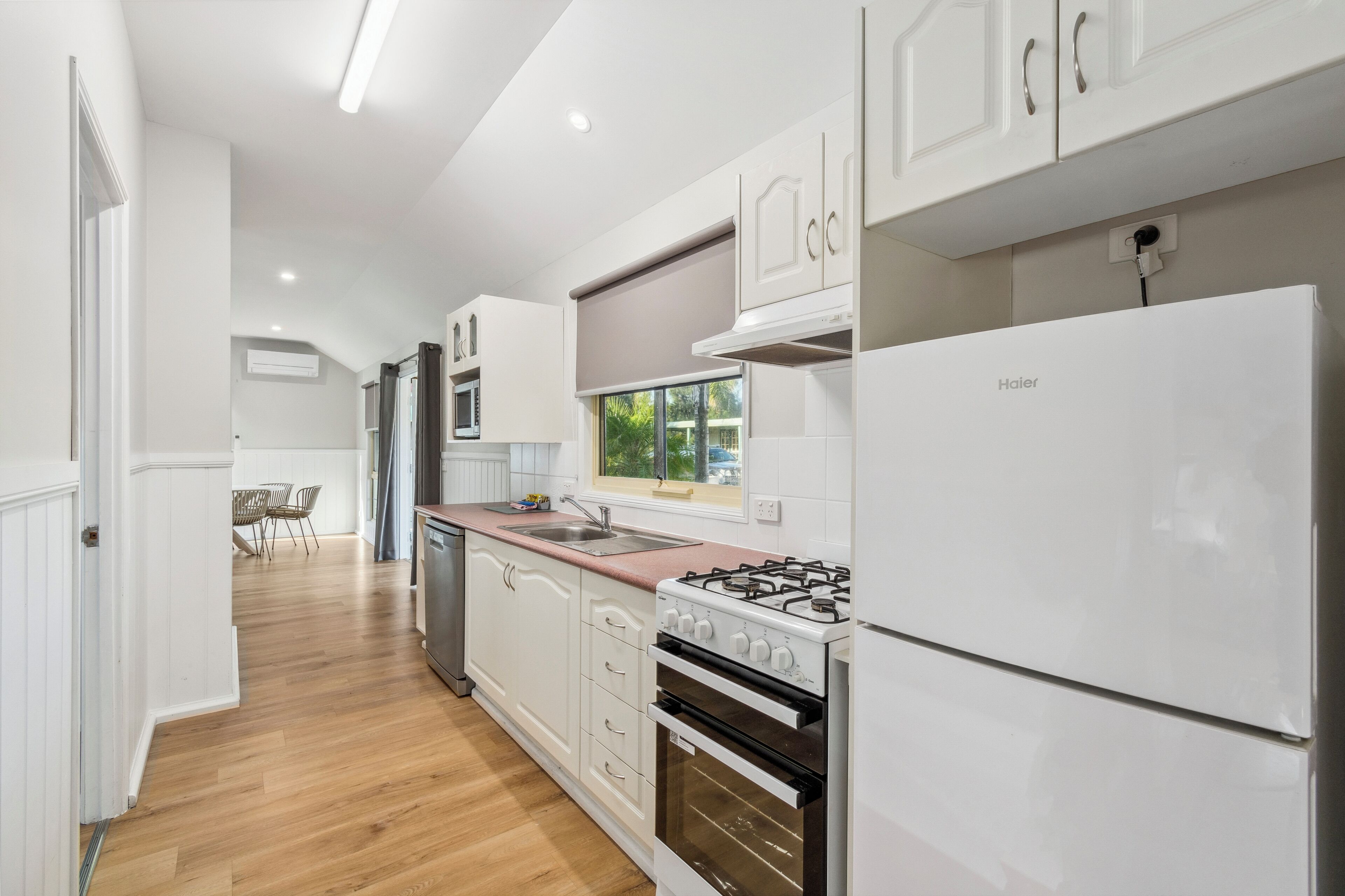A modern kitchen with white cabinets, a gas stove, a refrigerator, and a window with a view of greenery.