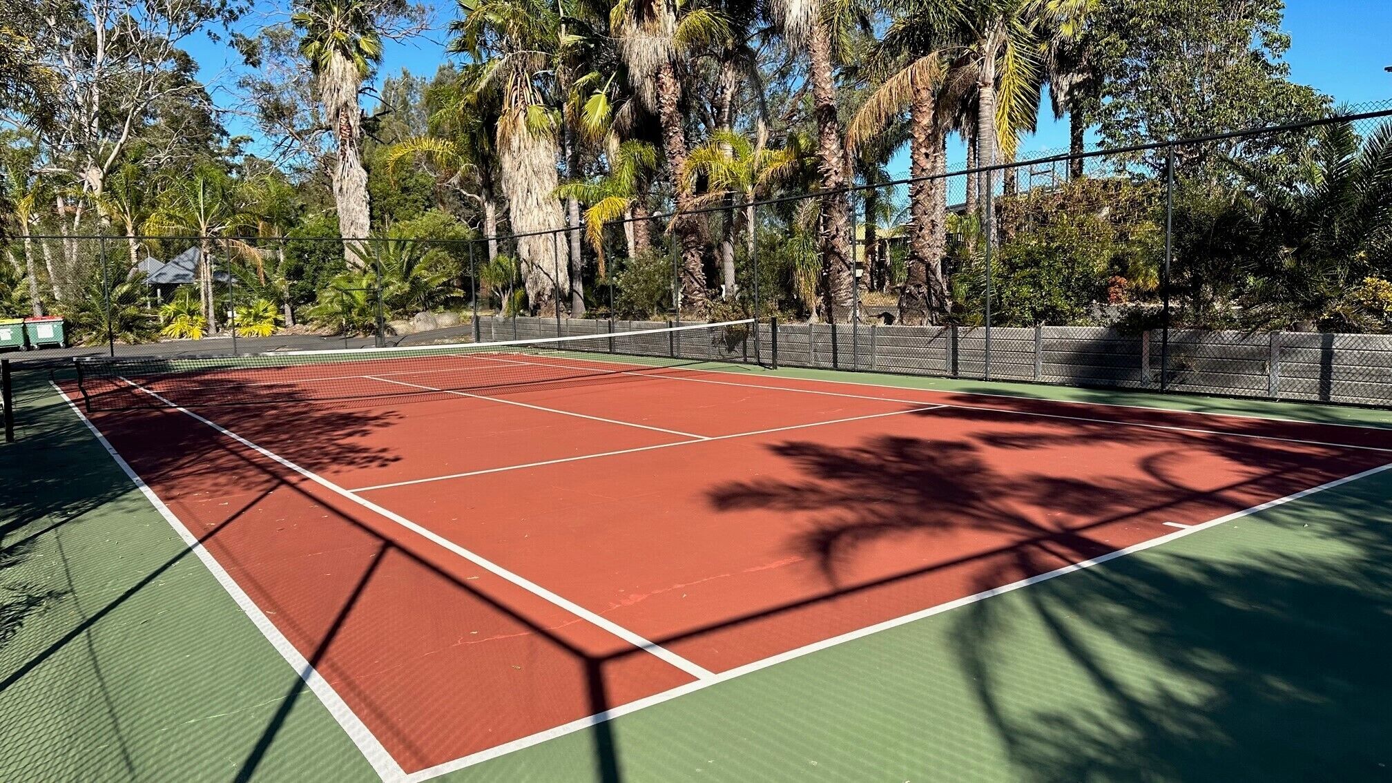 Un court de tennis entouré d’arbres et d’une clôture.