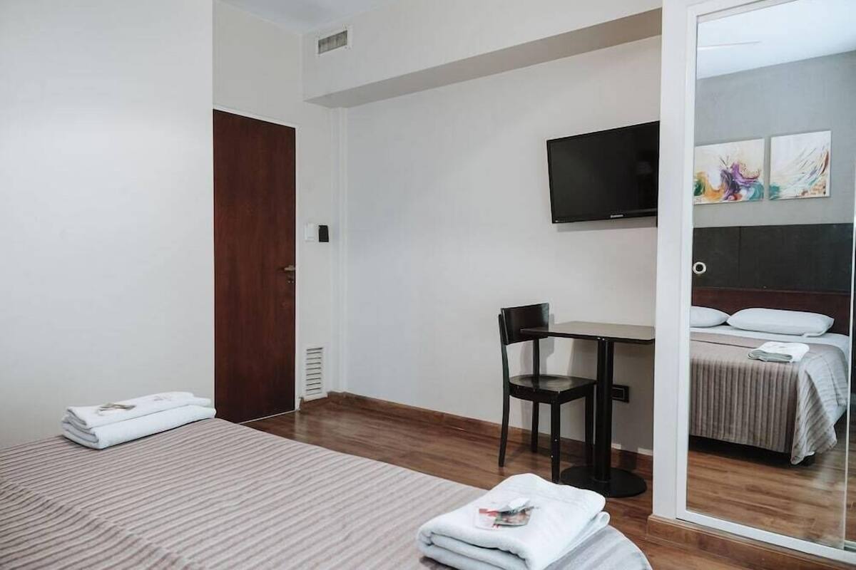 A hotel room with a bed, a desk, a chair, a TV, and a mirror.